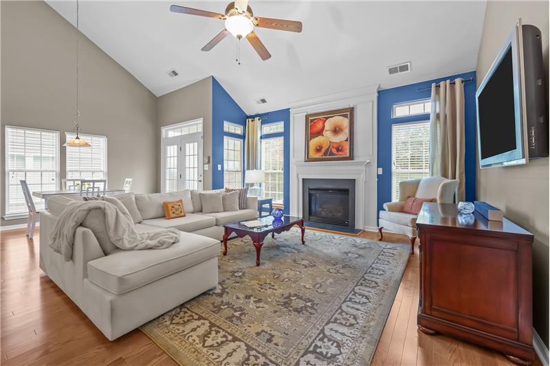 Expansive great room features gas fireplace with decorative mantel, vaulted ceiling, French-style windows