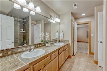 Basement Bathroom with dual sink vanity, mirror, and tiled tub/shower.