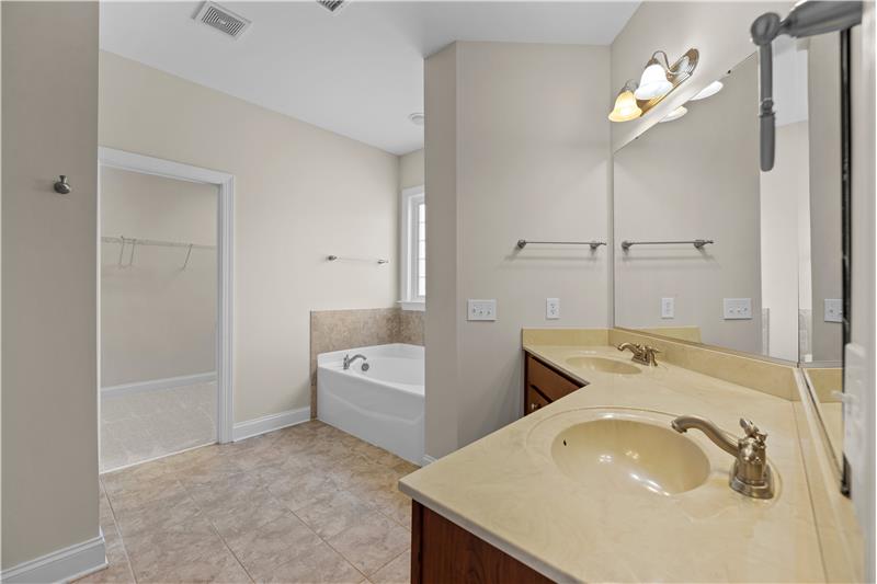 Primary bathroom has double-sink vanity with storage, tile floors, large walk-in closet.