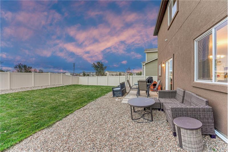 Sunset view of fenced level backyard with auto sprinklers, grass, and concrete patio.