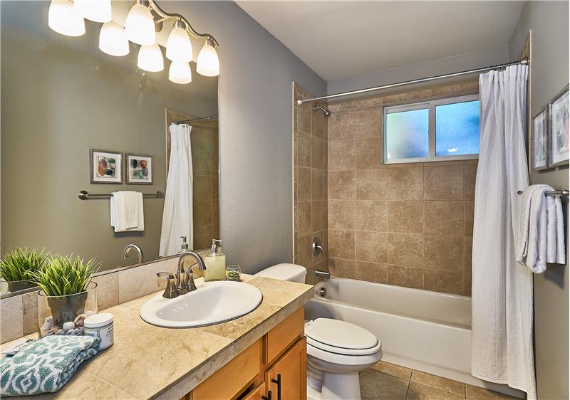 Full Sized Bathroom with Tile Surround Bathtub, Tile Floors, Maple Cabinets, Custom Light Fixtures and Tile Countertops.