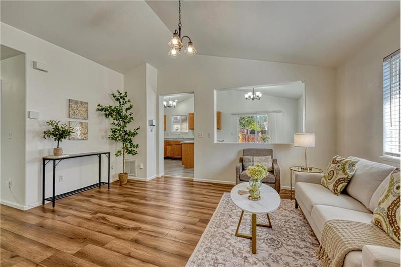 Spacious vaulted living room, featuring durable LVP floors, an attractive light fixture, & convenient coat closet.