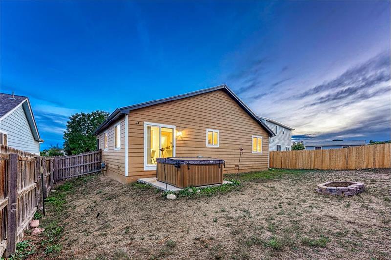 Large fenced backyard with sprinkler system, patio, raised flower bed, and hot tub.
