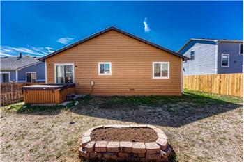 Rear view of home and backyard with raised flower bed, concrete patio, and hot tub.