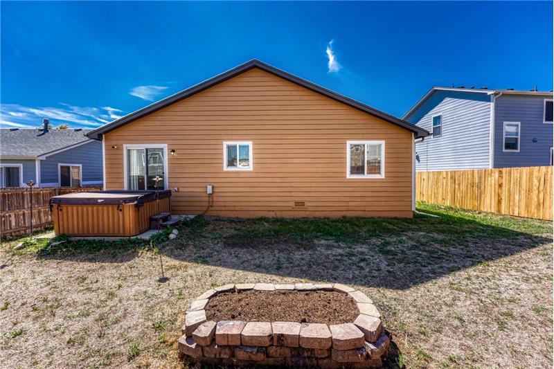 Rear view of home and backyard with raised flower bed, concrete patio, and hot tub.