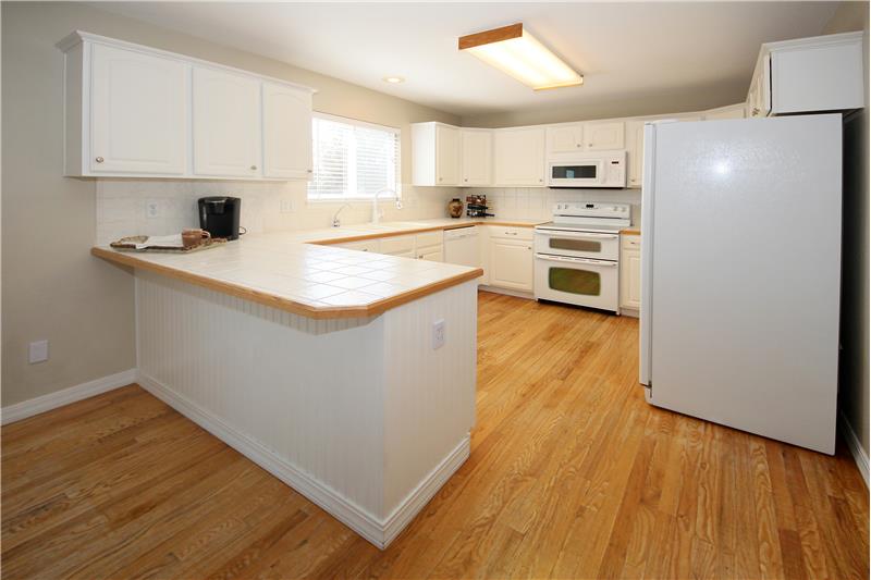 Functional kitchen with hardwood flooring, tile counter tops, and tile backsplash