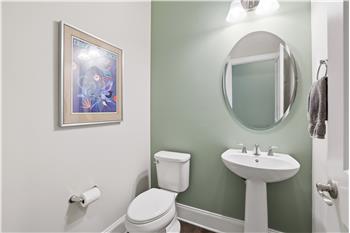 Pretty half bath with hardwood flooring, accent wall, pedestal sink.