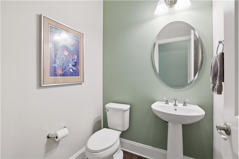 Pretty half bath with hardwood flooring, accent wall, pedestal sink.