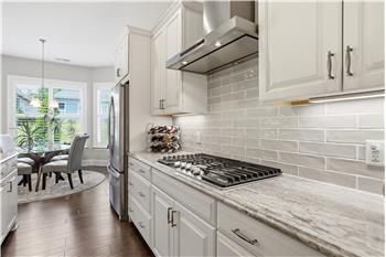 Crisp, white cabinetry plus gas cooktop, integrated wall oven/microwave and full-height tile backsplash add a polished finish.