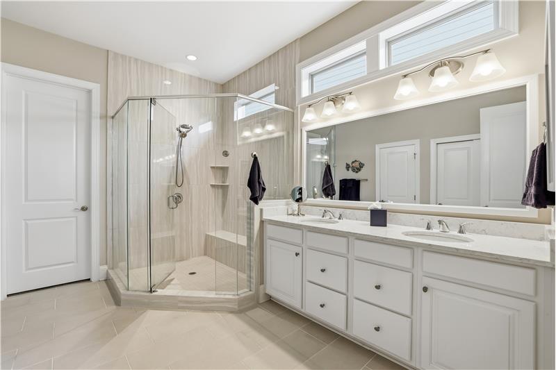 Primary bathroom has double sink vanity; oversized, glass shower with bench & tile surround; tile floors; walk-in closet.