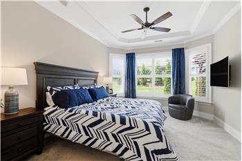Generous windows with plantation shutters and soft neutral tones give the primary bedroom an airy feel.