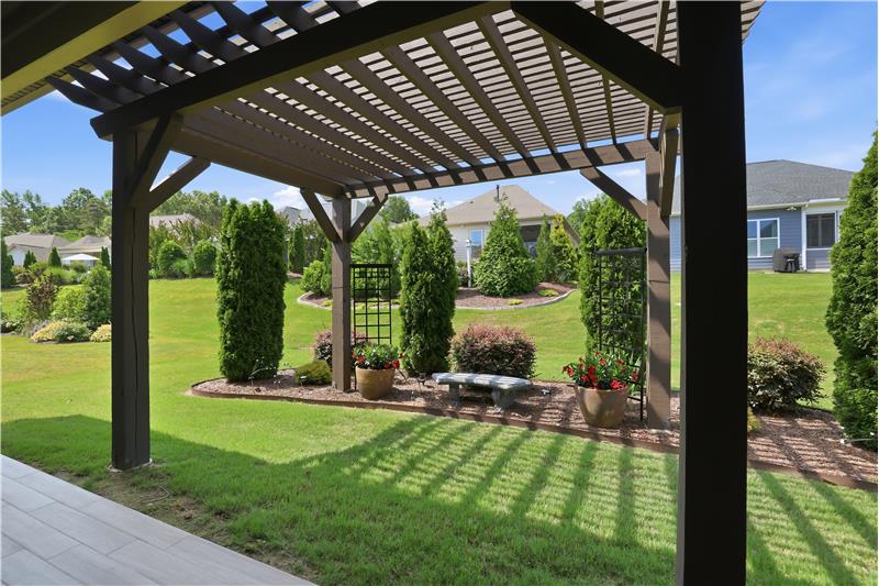 Covered patio extends to a pergola with landscaped surroundings.
