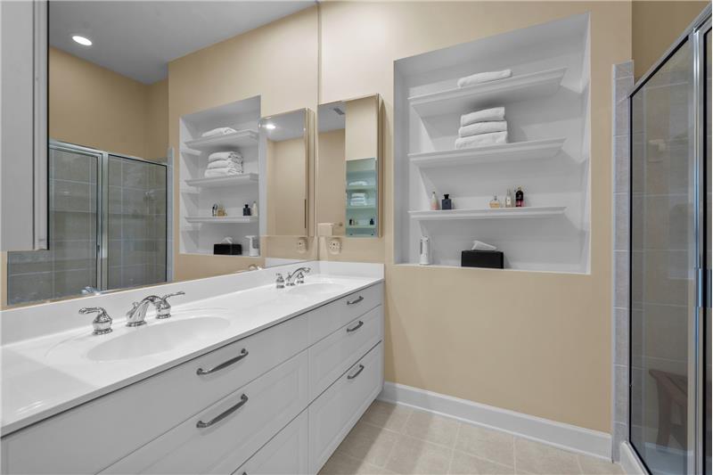 En-suite bathroom features double sink vanity with drawer storage, wall-mounted, mirrored medicine cabinets, tile flooring