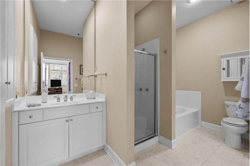 Bathroom accessed from the hallway and as an en-suite from second bedroom, featuring tile floors, storage, step-in shower, tub