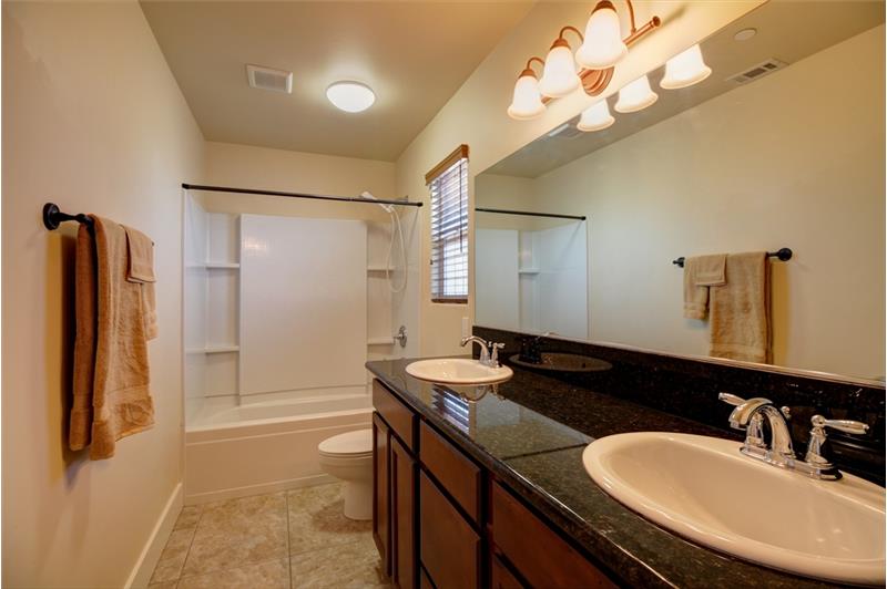 Full shower and tub surround w/integrated shelving, tile floors, more wood cabinets for storage, granite vanity & dual sinks.