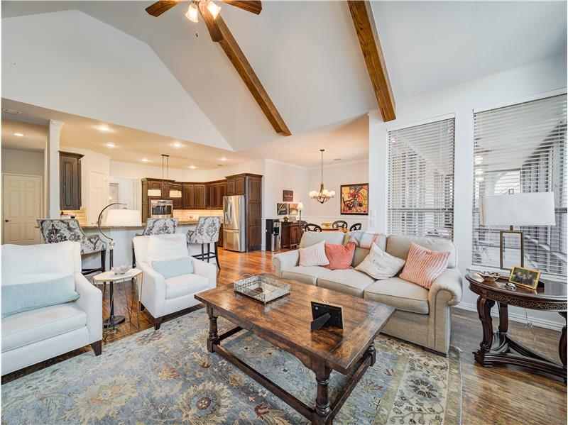 Living room with hardwood / wood-style floors, beam ceiling, ceiling fan with notable chandelier, and high vaulted ceiling