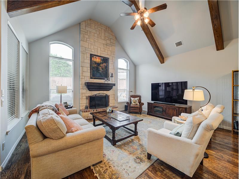Living room with beam ceiling, ceiling fan, a fireplace, and dark wood-type flooring