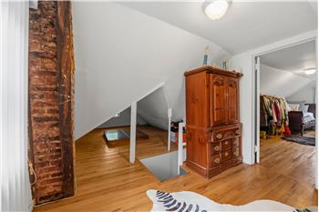Exposed brick structural column, wood-finish flooring, vaulted ceiling, and flush-mount ceiling lighting