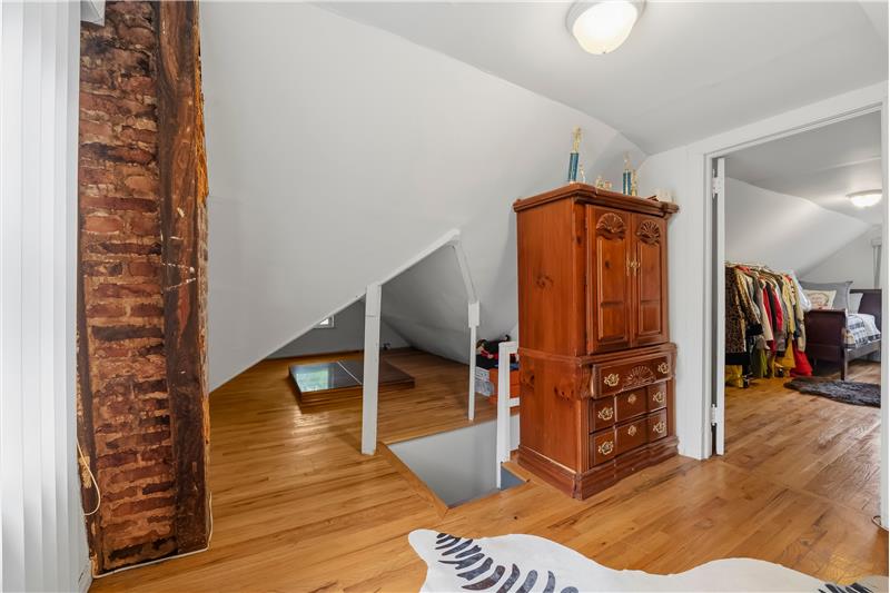 Exposed brick structural column, wood-finish flooring, vaulted ceiling, and flush-mount ceiling lighting
