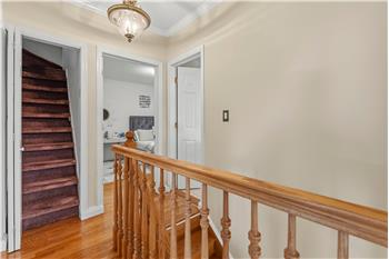 Staircase landing featuring wood-finish flooring, a traditional wood spindle railing, crown molding, and a flush-mount ceiling l