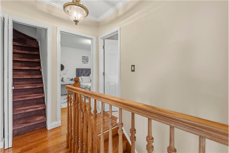 Staircase landing featuring wood-finish flooring, a traditional wood spindle railing, crown molding, and a flush-mount ceiling l
