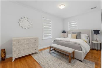 Bedroom featuring polished wood-finish flooring, two windows with horizontal blinds, a six-panel door, and a square glass-shade