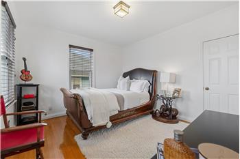 Bedroom featuring polished wood-finish flooring, two windows with horizontal blinds, a six-panel door, and a square glass-shade