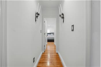Hallway leading to Primary Bedroom suite featuring wood-finish flooring and two black metal wall-mounted sconces