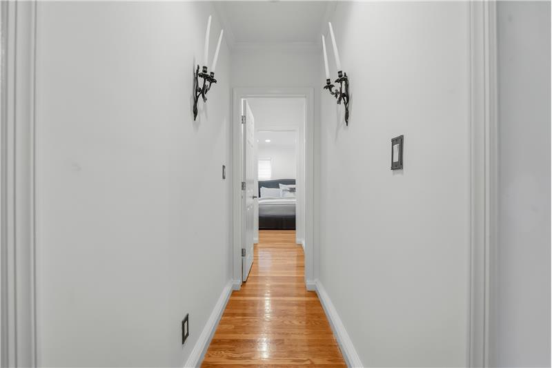 Hallway leading to Primary Bedroom suite featuring wood-finish flooring and two black metal wall-mounted sconces