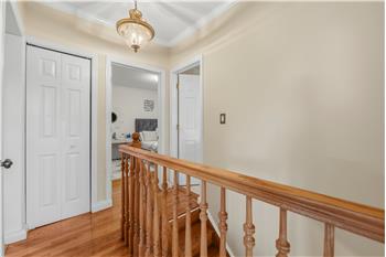 Hallway featuring wood-finish flooring, a bi-fold closet, a wooden railing with balusters, crown molding, and a traditional pend