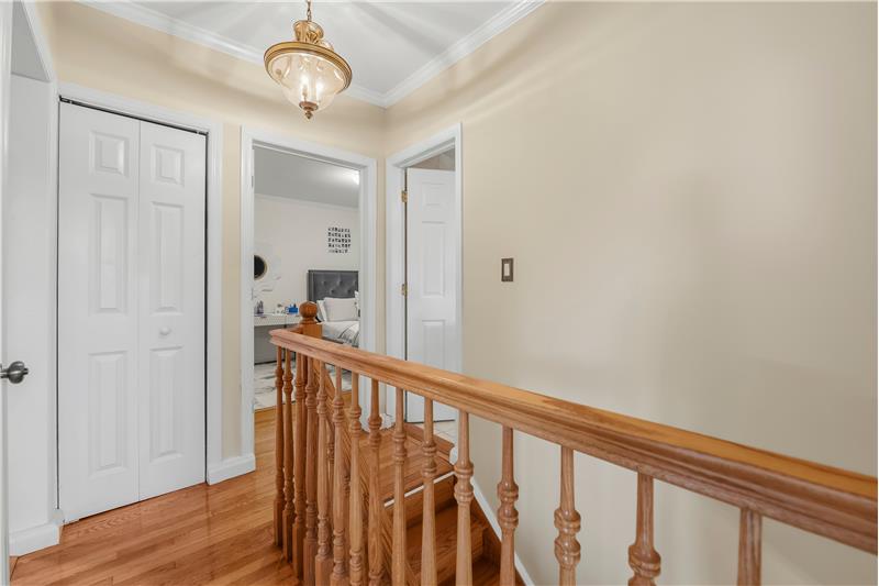 Hallway featuring wood-finish flooring, a bi-fold closet, a wooden railing with balusters, crown molding, and a traditional pend
