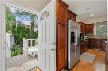 Kitchen featuring rich wood cabinetry, stainless steel refrigerator, dark stone countertops, wood-finish flooring, and exterior