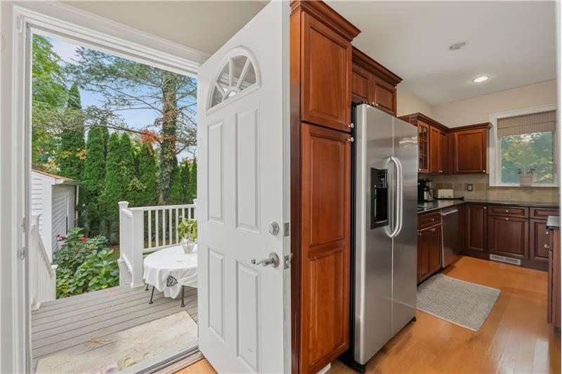 Kitchen featuring rich wood cabinetry, stainless steel refrigerator, dark stone countertops, wood-finish flooring, and exterior