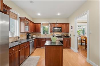 Kitchen featuring wood cabinetry, stone countertops, a center island, stainless steel appliances, and wood-finish flooring