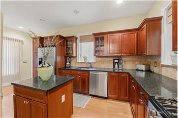 Kitchen featuring warm-tone cabinetry, stone countertops, stainless steel appliances, a central island, and recessed lighting