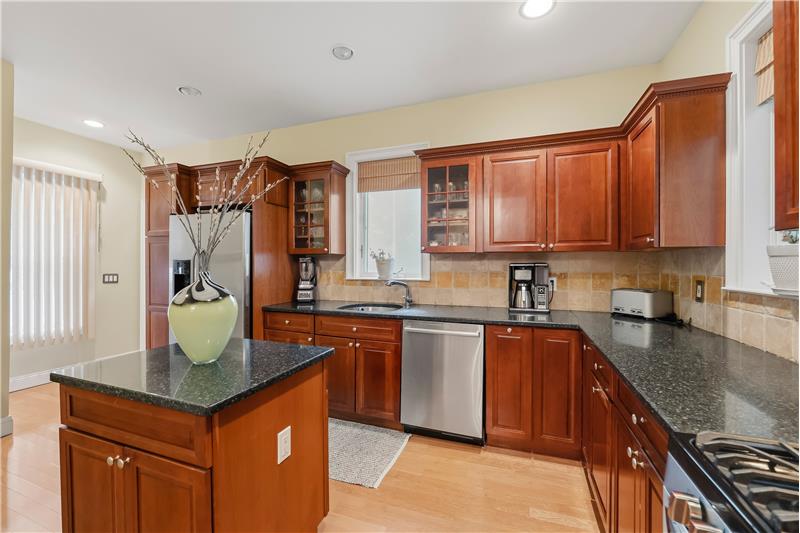 Kitchen featuring warm-tone cabinetry, stone countertops, stainless steel appliances, a central island, and recessed lighting