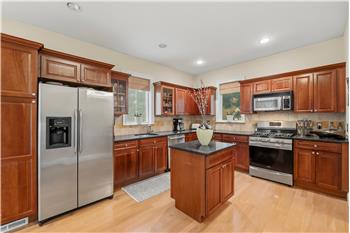 Kitchen featuring warm-toned wood cabinetry, granite countertops, stone tile backsplash, stainless steel appliances, and a cente