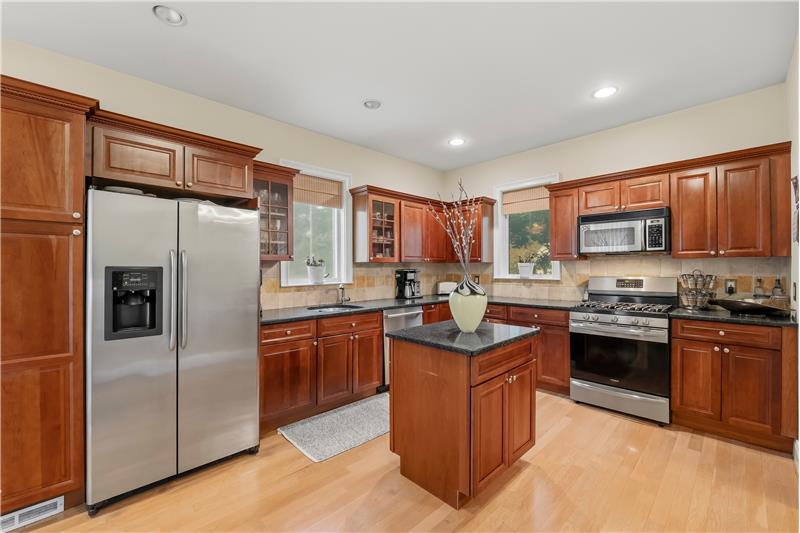 Kitchen featuring warm-toned wood cabinetry, granite countertops, stone tile backsplash, stainless steel appliances, and a cente
