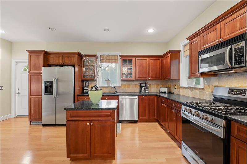 Kitchen featuring warm-toned wood cabinetry, granite countertops, stone tile backsplash, stainless steel appliances, and a cente