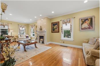 Living room featuring wood-finish flooring, recessed lighting, crown molding, and a fireplace with a stone surround