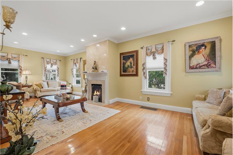 Living room featuring wood-finish flooring, recessed lighting, crown molding, and a fireplace with a stone surround