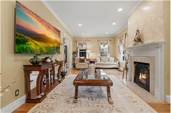 Living area featuring wood-finish flooring, recessed lighting, crown molding, and a fireplace with a stone surround and decorati