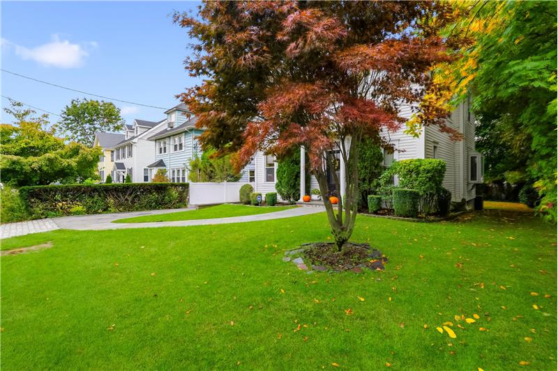 Multi-story light-colored siding exterior with a manicured front lawn, curved paver walkway, mature landscaping