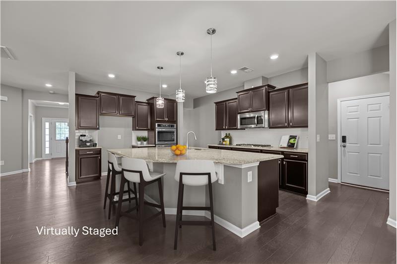 Kitchen features large granite island with seating, pendant lighting rich espresso cabinetry for a modern yet timeless look