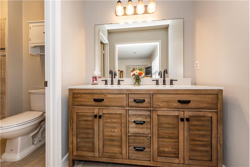 En-suite bathroom in owner's bedroom has brand new vanity with dual sinks, new faucets, updated light fixture.