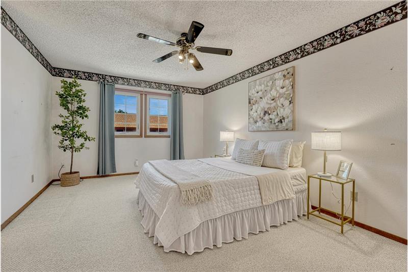 The spacious upper level primary bedroom is a private retreat that features neutral carpet and a lighted ceiling fan.