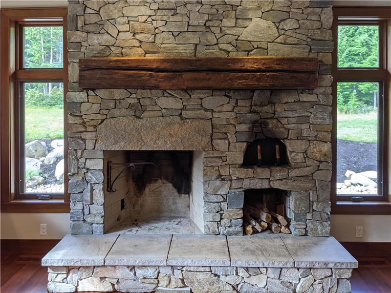 Genuine stone, Rumford wood fireplace with iron kettle handle, wood storage & pizza oven. Wood beam is reclaimed wood.