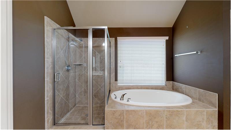 An oval bathtub with a separate glass enclosed tile shower.