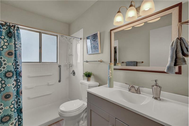 Main level shower bathroom with new vanity, countertops, mirror, lights and toilet