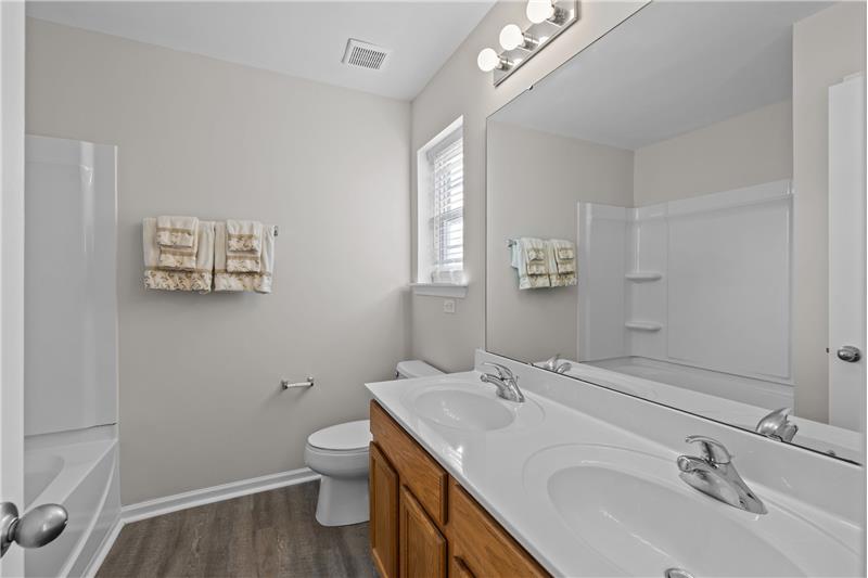 En-suite bathroom with double sink vanity, new tub/shower surround, window providing natural light.